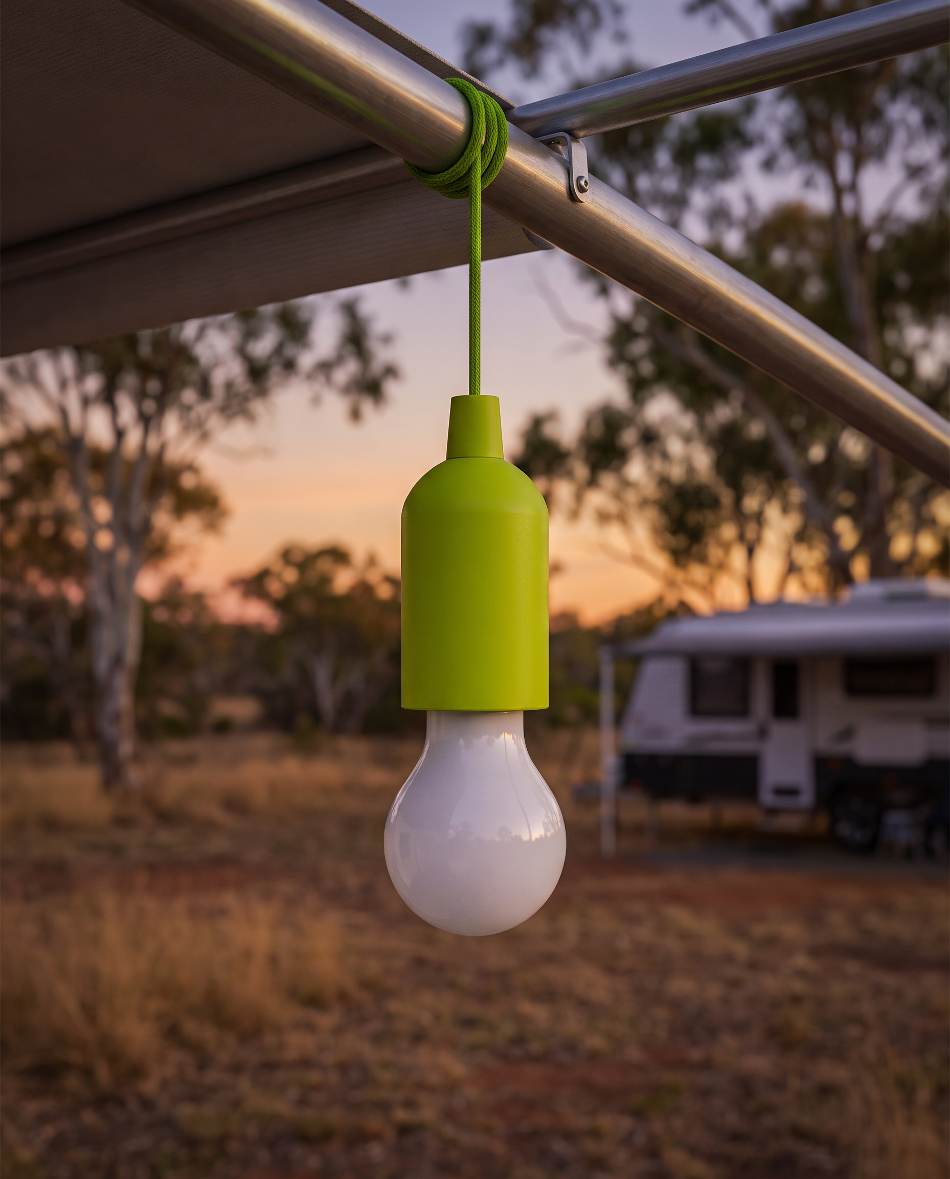 Green LED pull camping light hanging from a caravan awning rail at dusk